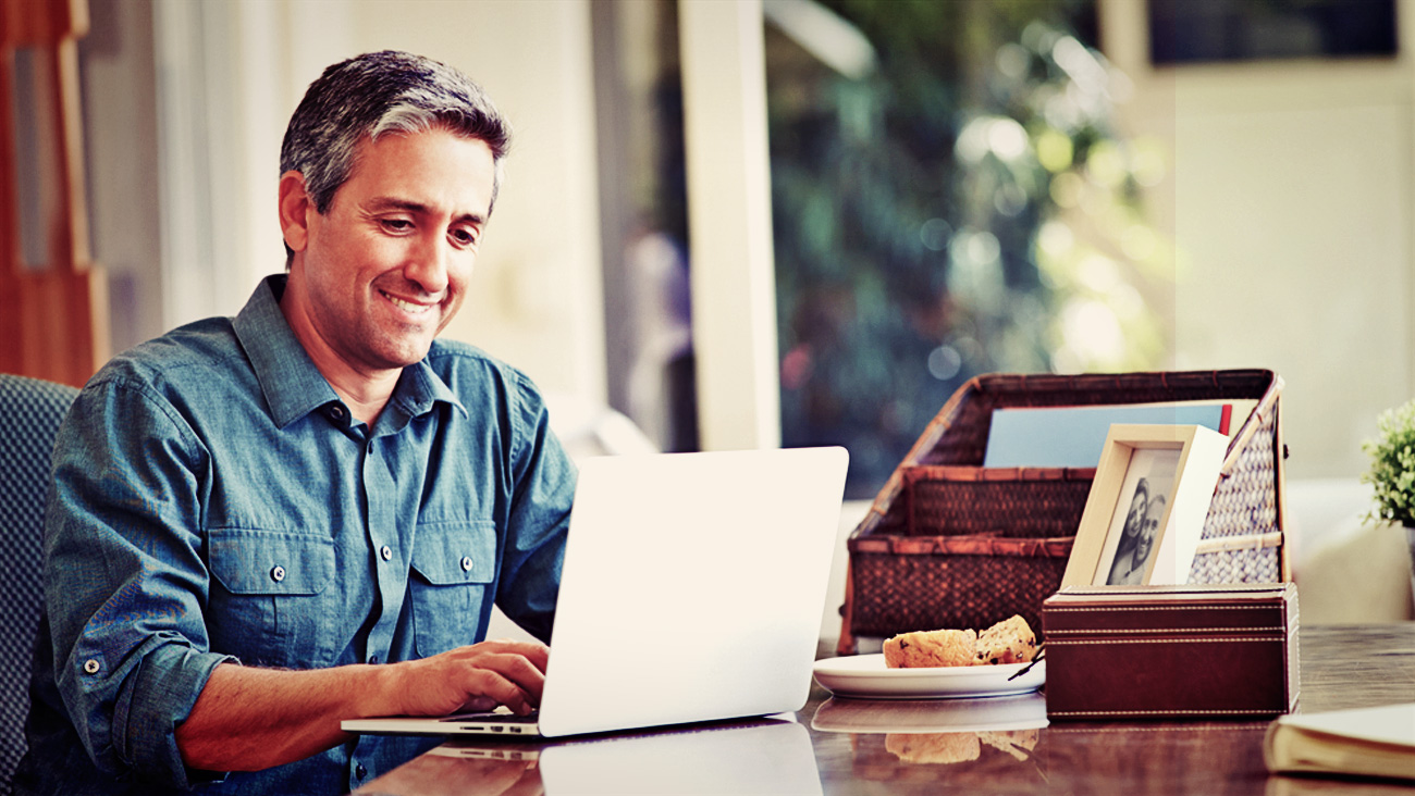 Imagem de um homem grisalho sorrindo administrando pelo computador - Gestão de Condomínios